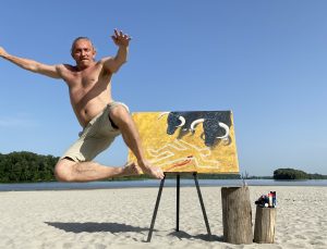 Emerging artist jumps in celebration in front of the "Crime Scene" provocative bull painting on a sandy beach by the Danube River.