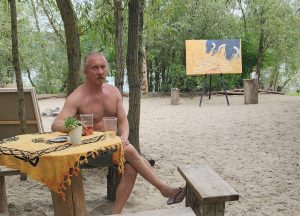 rtist relaxing at a beach bar with the "Crime Scene" provocative bull painting in the background. The artwork depicts a bullfighting scene.