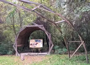 "Karate Bull" surreal flying bull painting displayed on an easel under a roof in a forest setting.