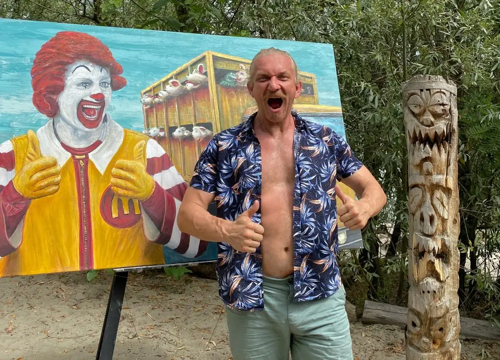 Artist mimics Ronald McDonald's pose in front of the "Casual Cruelty" surreal animal rights painting, highlighting the connection between fast-food mascots and animal cruelty.