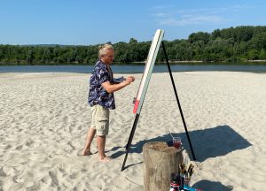 Artist painting "Death in the Afternoon," a disturbing artwork depicting a toreador and fallen bulls, on a sandy beach during a summer day.